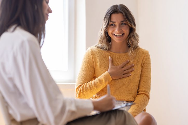 woman in yellow shirt with hand over chest happily talking with a counselor